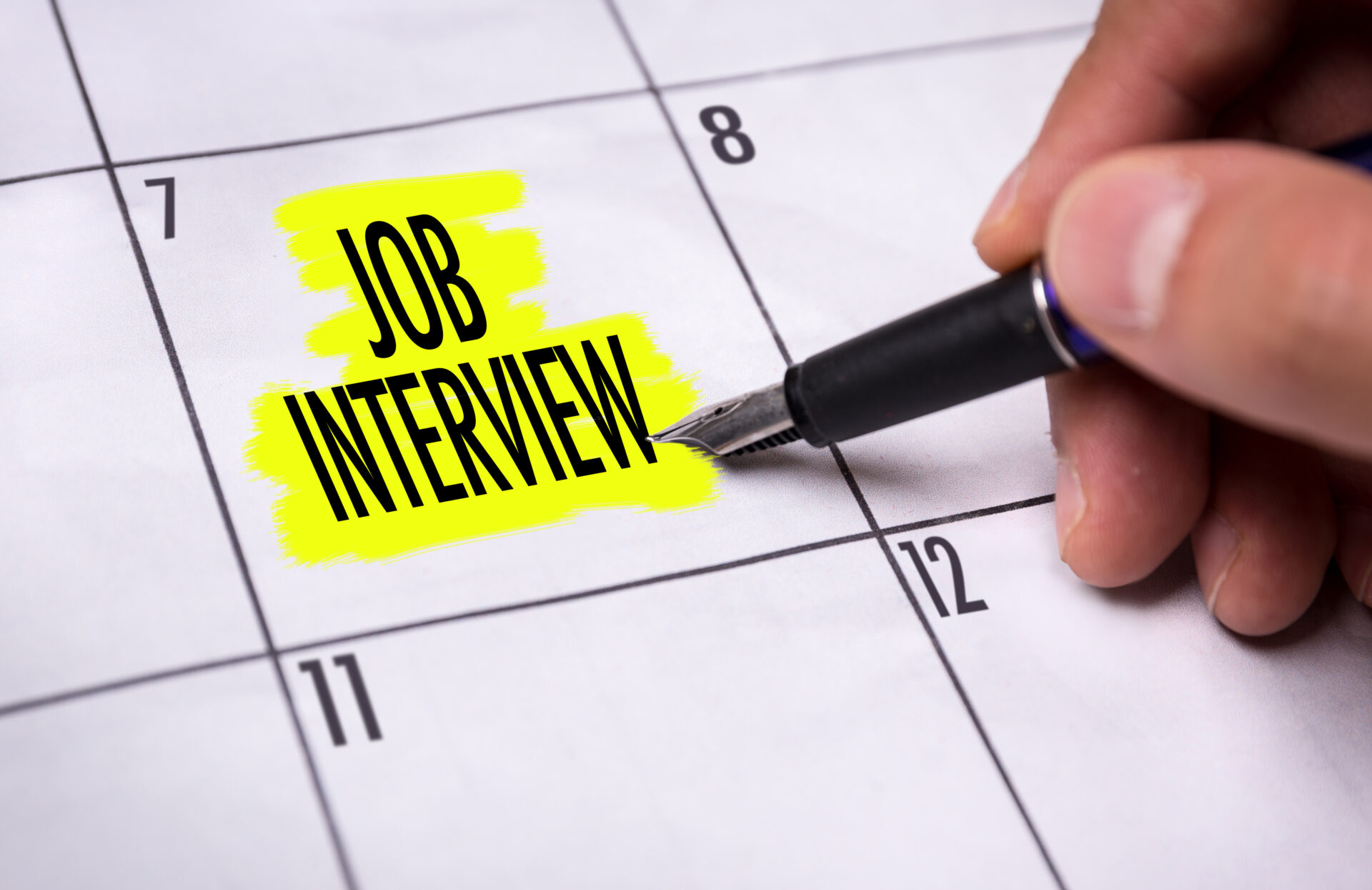 paper calendar with the words "job interview" written and highlighted on a date, and a white hand with a highlighter marking the words