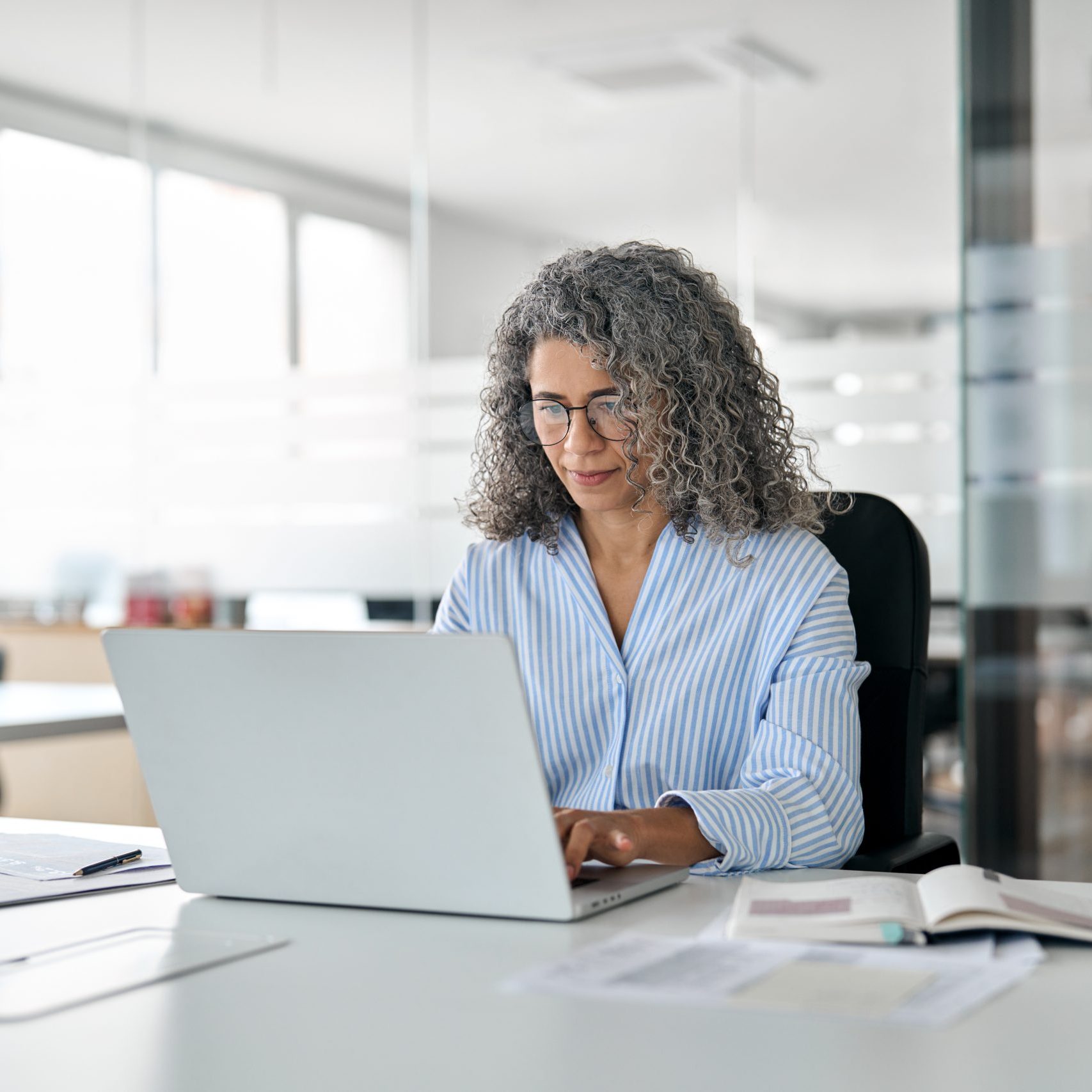Busy mature professional business woman looking at laptop working in office.